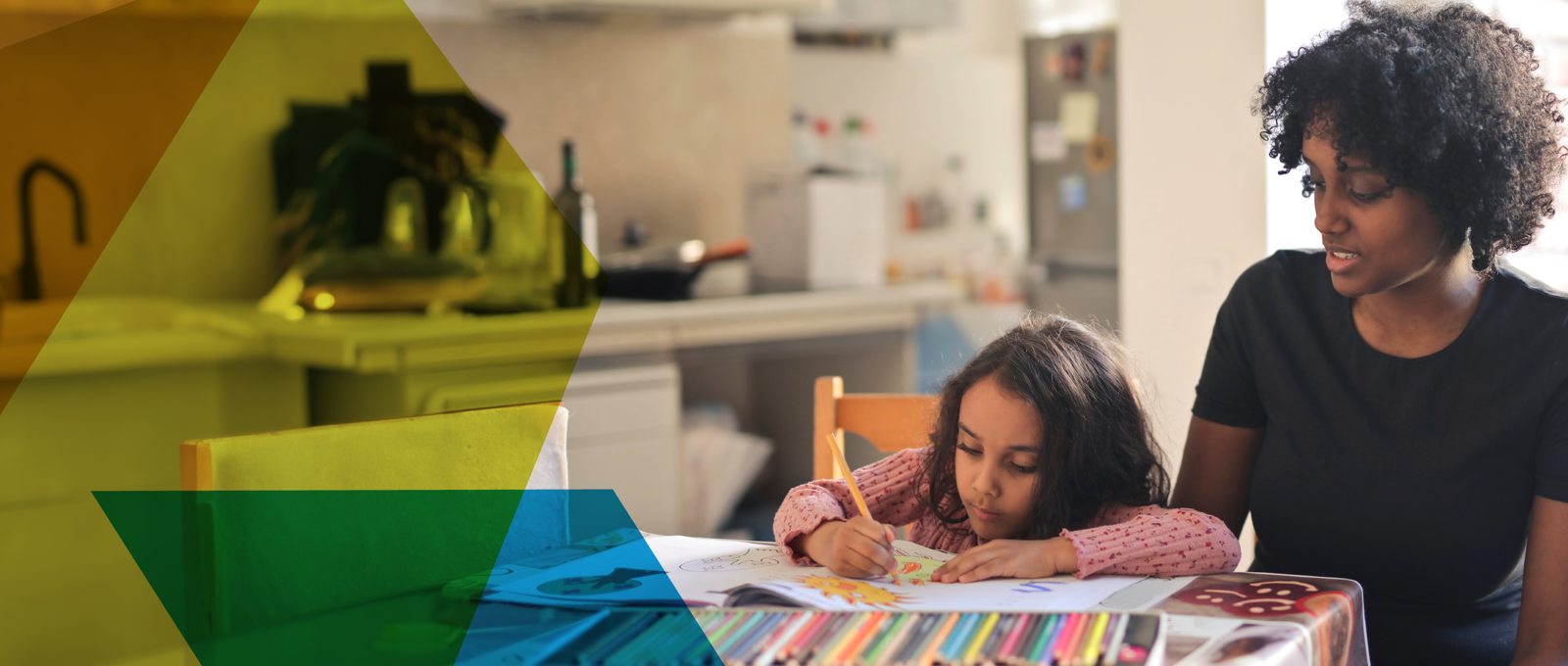 Mother observes daughter colouring notebook while sitting at a table in their kitchen