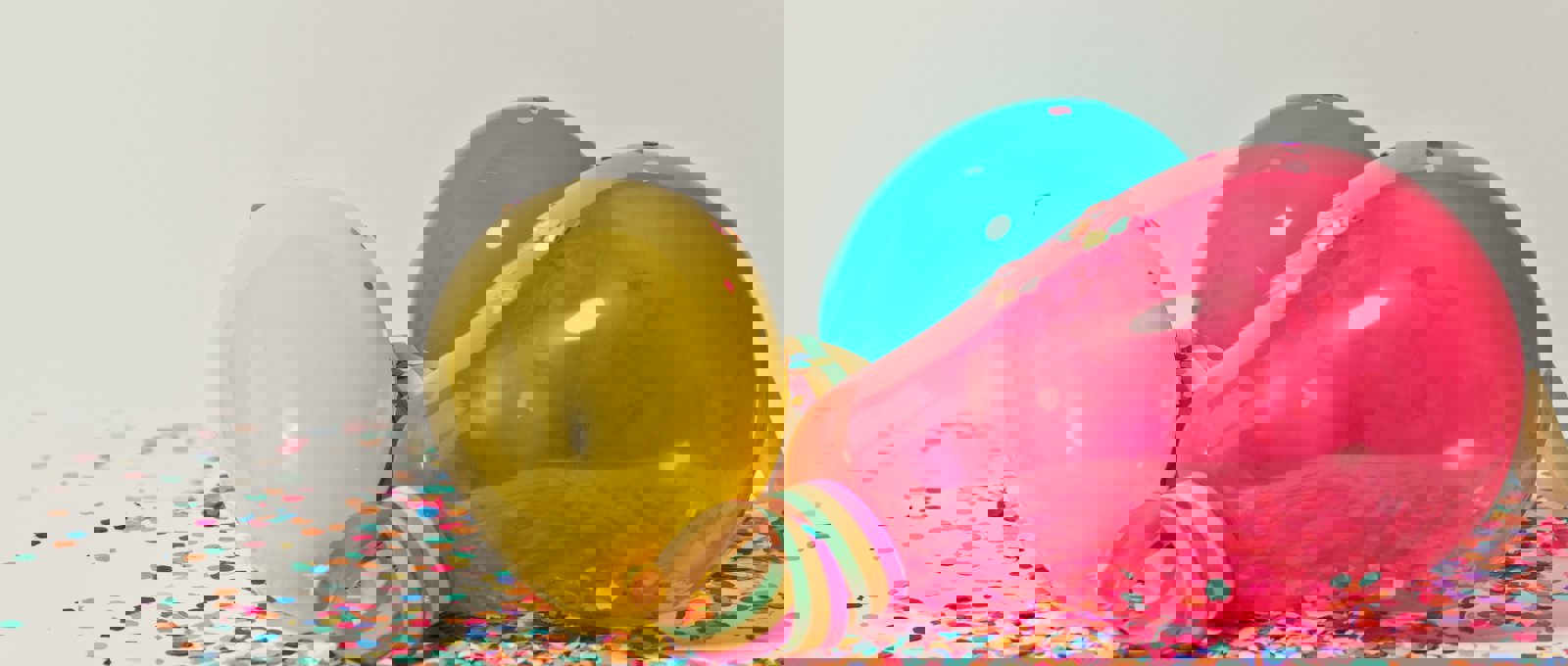 Yellow, teal and pink balloons against a confetti background.
