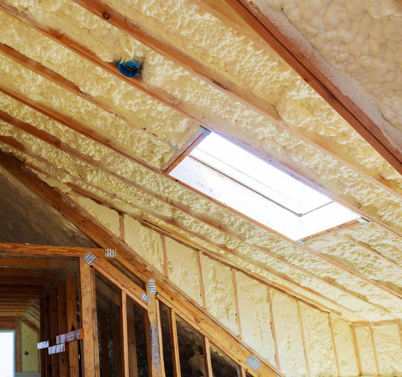 Photo of a loft, with rolls of cream insulation put into the roof. There are wooden panes and a window.