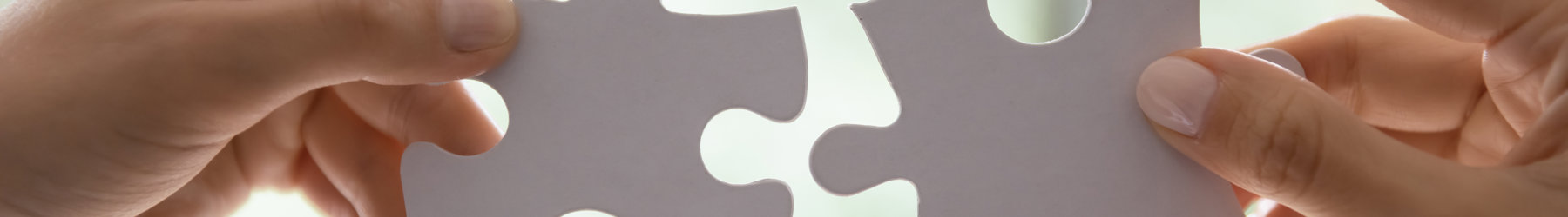 Two hands, each holding a large white jigsaw piece connecting them together