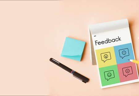 Photograph taken from overhead of someone holding a pencil to write on a notepad which is headed 'Feedback'