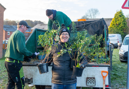 Photo of a Futures employee holding two plants and smiling at the camera as he helps to unload a truck
