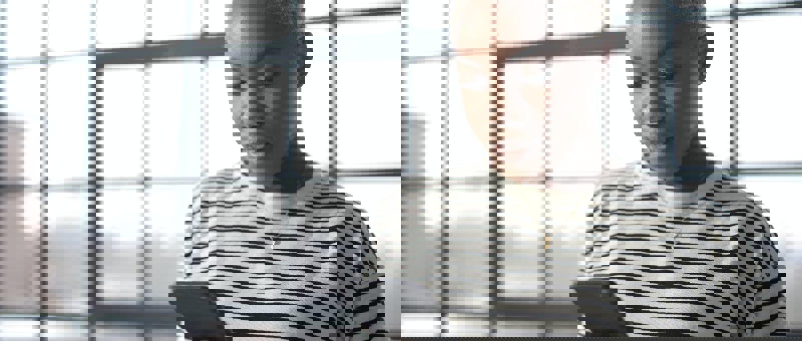 Photo of a young black woman with bleached hair looking at her phone. She is standing in front of a large window.