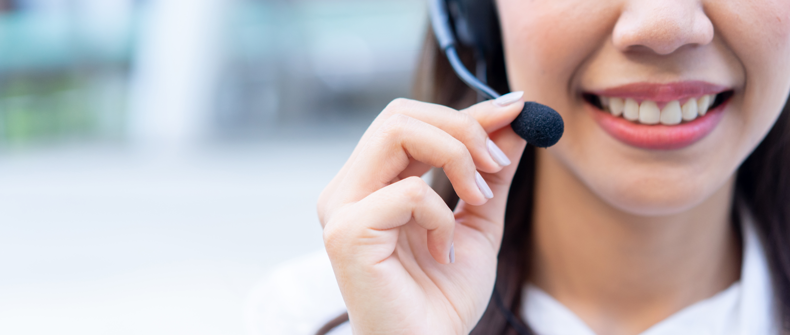 Close up photo showing the lower half of a woman's face. She is smiling and wearing a telephone headset. She is holding the microphone part with her right hand