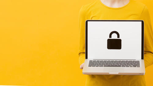 Photograph of a woman wearing yellow clothes against a yellow background. She is holding a laptop. On the screen is a padlock symbol.