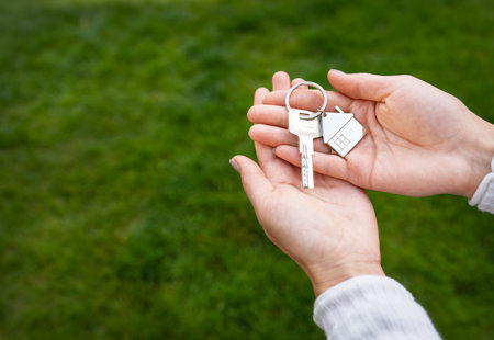 Keys With Keychain Form Metal House From New House Apartment Hands Girl Against Background Green Grass
