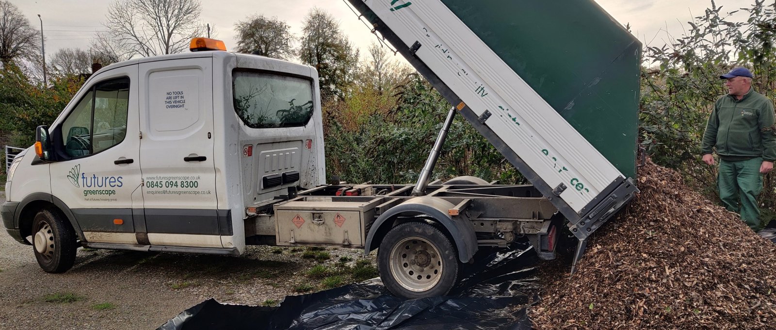 Photograph of an open back truck unloading a pile of tree bark chippings onto the ground