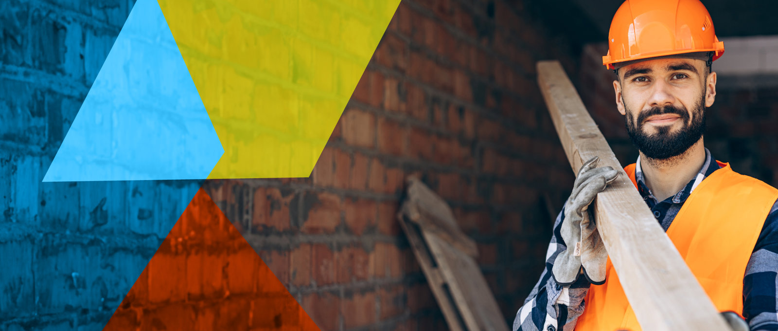 Photo of a smiling construction worker in protective clothing inside a property under construction. He is smiling, looking at the camera and supporting a long piece of timber on his shoulder.