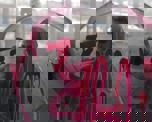 Photo of a man in sunglasses and a hoodie spraying red graffiti on glass - viewed from the other side of the glass