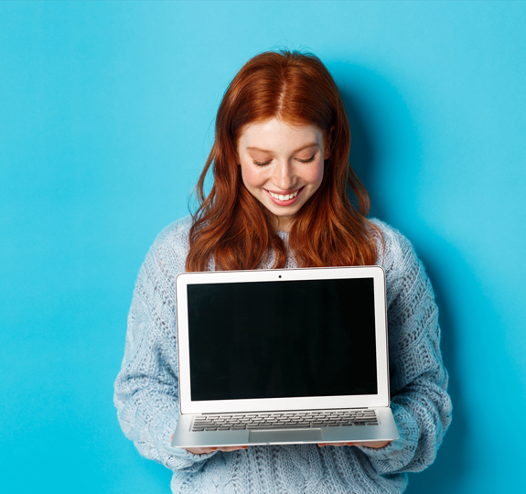 Red-haired smiling woman holding and looking down on an open laptop with the screen facing away from her. 